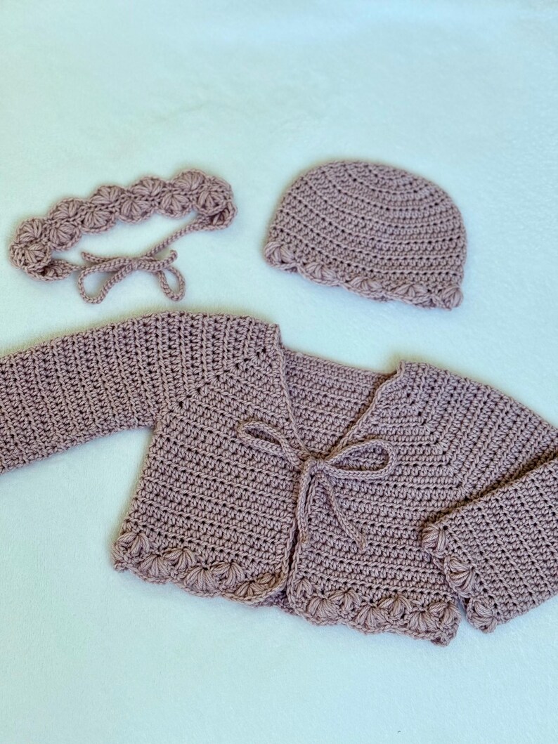 Pu&ograve; includere: Un set per neonati all'uncinetto fatto a mano, color malva, composto da un cardigan, un cappellino e una fascia. Il cardigan ha maniche lunghe e chiusura con fiocco. Il cappellino e la fascia presentano un bordo smerlato. Il set &egrave; realizzato in filato morbido.