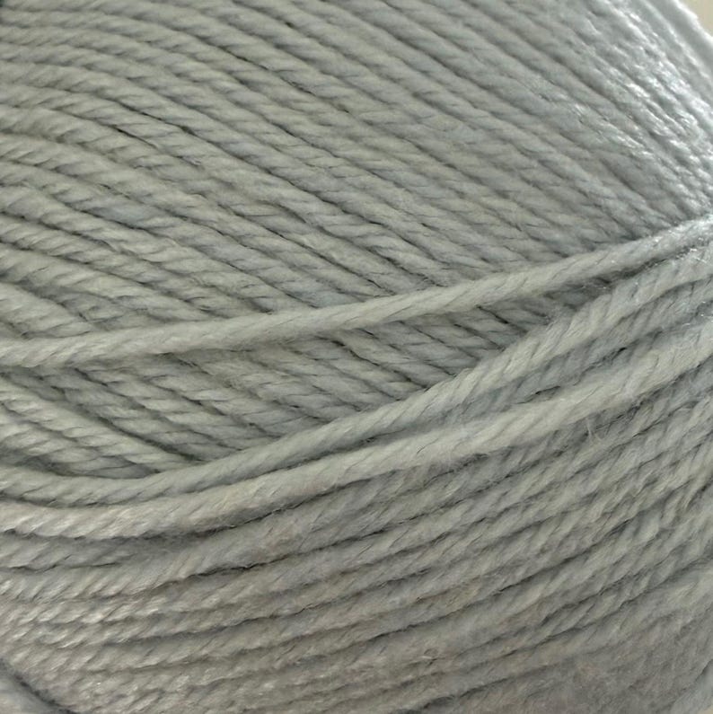 Puede incluir: Primer plano de una madeja de hilo azul claro. El hilo est&aacute; bien enrollado, mostrando hebras individuales con una apariencia texturizada. El color es un azul suave y apagado, adecuado para proyectos de tejido o ganchillo.
