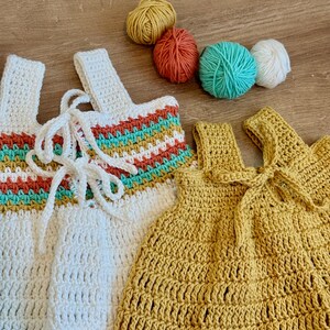 May include: Two handmade crochet tops, one white with rainbow stripes and the other yellow, are displayed. The white top has a laced front, while the yellow one has a bow. Four balls of yarn in yellow, orange, teal, and white are also visible.