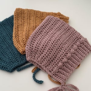 Puede incluir: Tres gorros de ganchillo hechos a mano en verde azulado, marr&oacute;n y malva. Cada gorro presenta un patr&oacute;n de puntada texturizada y lazos en la barbilla. Los gorros est&aacute;n hechos de hilo suave y son adecuados para beb&eacute;s y ni&ntilde;os peque&ntilde;os.