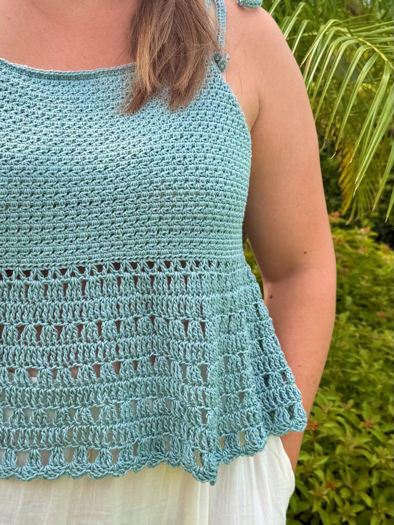Pu&ograve; includere: Un top all'uncinetto azzurro caratterizzato da un fitto motivo a punti strutturati sul corpetto superiore e da un design in pizzo traforato a contrasto sulla parte inferiore svasata. Il capo presenta sottili spalline regolabili.