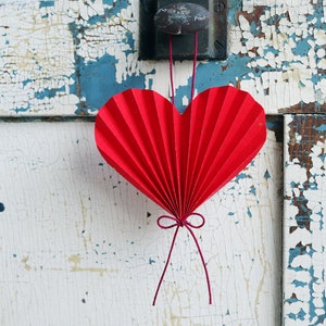 May include: A red paper heart hanging from a doorknob on a white and blue weathered wooden door.