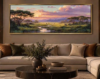 Puede incluir: Un cuadro panorámico de paisaje en un marco dorado que representa una sabana africana al atardecer con acacias, un arroyo serpenteante y montañas lejanas bajo un cielo lleno de nubes rosas y naranjas, montado en una pared sobre un sofá beige.