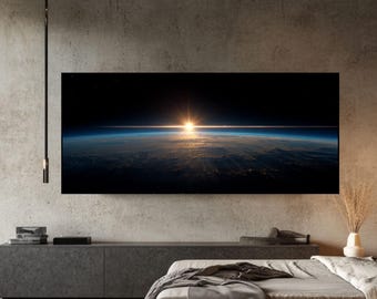 May include: A large rectangular canvas print depicting a sunrise over Earth from space. The image features a vibrant orange sun, a blue and white atmosphere, and a dark expanse of space. The print is mounted on a gray wall above a bed.