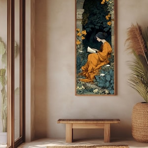 May include: A vertical rectangular wall art print featuring a person in a flowing orange robe sitting and reading a book within a dark stone archway surrounded by lush green foliage and clusters of vibrant yellow flowers in a garden setting.