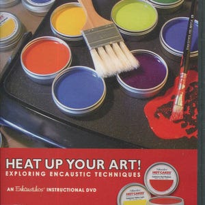 Op de afbeelding: Een instructie-dvd getiteld "Heat Up Your Art!" met encaustic technieken. De afbeelding toont verschillende kleuren "Hot Cakes" encaustic wasverf in kleine metalen blikken, samen met penselen. Kleuren zijn onder meer rood, geel, groen en blauw.
