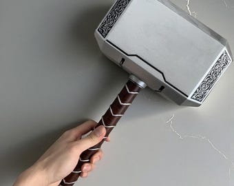 May include: A silver and black hammer with intricate designs on the head and a brown handle. The hammer's head is rectangular with decorative patterns on the edges. The handle is wrapped in brown leather-like material.