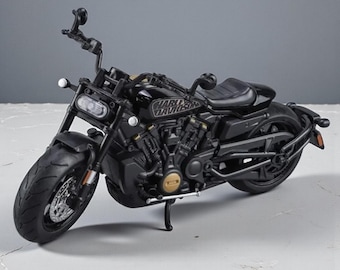 May include: A black Harley-Davidson motorcycle model. The model features a detailed design, including the Harley-Davidson logo, a black seat, and a front headlight. The motorcycle is displayed on a neutral gray surface.