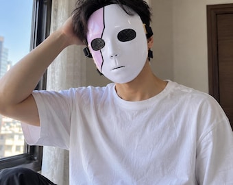 May include: A full-face mask featuring a smooth white surface with a vertical light pink stripe on the left side. The mask includes black mesh eye coverings and is secured with black elastic straps that wrap around the sides of the head.