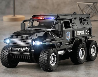 May include: A black toy police armored vehicle with six wheels, headlights, and a red and blue light bar. The vehicle has the word "POLICE" in white and a badge on the side. The tires are large and rugged.