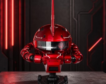 May include: A metallic red robot head bust featuring a prominent vertical fin on top, a wide horizontal visor with a circular lens detail, and segmented mechanical neck components mounted on a black hexagonal base with intricate panel line detailing.