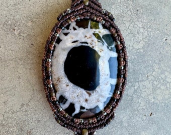 May include: A black and white agate stone pendant with a brown and black macrame cord. The stone has a unique pattern of white and black swirls.