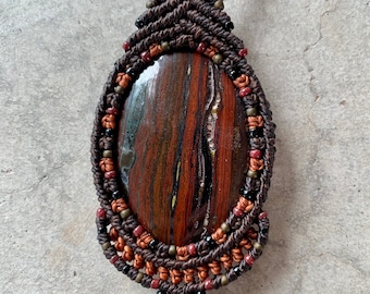 May include: A brown, black, and red beaded macrame necklace with a large, oval-shaped, red, brown, and black stone pendant.