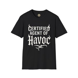 May include: Black t-shirt with the text "CERTIFIED AGENT OF HAVOC" in white, stylized lettering. The design includes flame-like accents above the words "CERTIFIED" and a decorative flourish below "HAVOC". The shirt has a crew neck and short sleeves.
