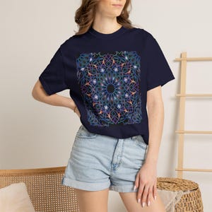 May include: A dark navy blue short-sleeve t-shirt featuring a large, centred graphic print. The design consists of a complex, symmetrical geometric mandala pattern in vibrant shades of neon blue, purple, and orange against a black background.