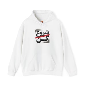 Puede incluir: Una sudadera con capucha blanca que cuenta con un bolsillo tipo canguro frontal y mangas largas. El centro del pecho muestra un gráfico con texto en escritura persa negra atravesado por un trazo de pincel rojo sobre un cuadrado gris.