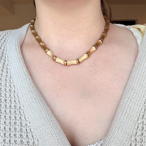 以下が含まれることがあります： 竹のデザインのゴールドトーンのネックレス。ネックレスは、より小さな金色のリングで接続された円筒形のセグメントが特徴です。竹スタイルのセグメントはテクスチャード加工されたマット仕上げで、リングは研磨されています。