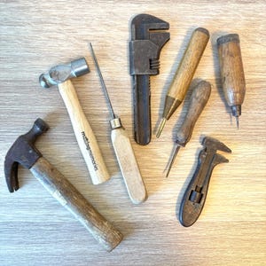 May include: A collection of vintage hand tools including two hammers, one with the text "making memories" on the handle, a metal adjustable wrench, two wooden-handled awls, a metal scribe, and a small metal adjustable wrench with a wooden handle.