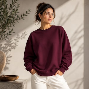 Puede incluir: Una sudadera de cuello redondo en color burdeos profundo s&oacute;lido, con mangas largas y pu&ntilde;os acanalados. La prenda presenta un corte relajado con un escote redondo cl&aacute;sico, ofreciendo una est&eacute;tica limpia y sencilla en un tono rojo oscuro.
