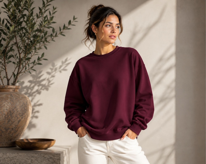 Puede incluir: Una sudadera de cuello redondo en color burdeos profundo s&oacute;lido, con mangas largas y pu&ntilde;os acanalados. La prenda presenta un corte relajado con un escote redondo cl&aacute;sico, ofreciendo una est&eacute;tica limpia y sencilla en un tono rojo oscuro.