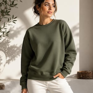 Puede incluir: Una sudadera de cuello redondo en color verde oliva con mangas largas y pu&ntilde;os acanalados, combinada con pantalones blancos. La sudadera presenta un dise&ntilde;o de color s&oacute;lido con un cuello redondo est&aacute;ndar y un corte holgado y sencillo.