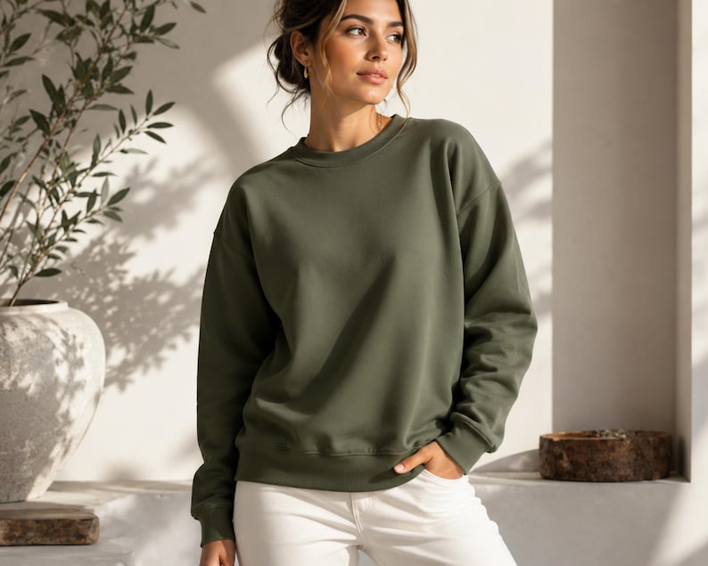Puede incluir: Una sudadera de cuello redondo en color verde oliva con mangas largas y pu&ntilde;os acanalados, combinada con pantalones blancos. La sudadera presenta un dise&ntilde;o de color s&oacute;lido con un cuello redondo est&aacute;ndar y un corte holgado y sencillo.