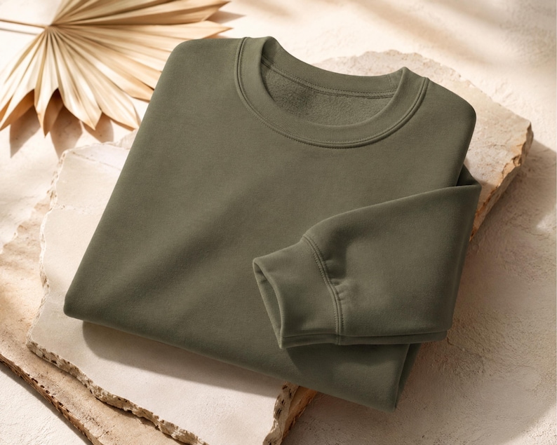Puede incluir: Una sudadera de cuello redondo en color verde oliva s&oacute;lido, con mangas largas de pu&ntilde;os acanalados y un cuello tambi&eacute;n acanalado. La prenda est&aacute; confeccionada en un tejido liso y opaco, con una textura interior similar al forro polar.
