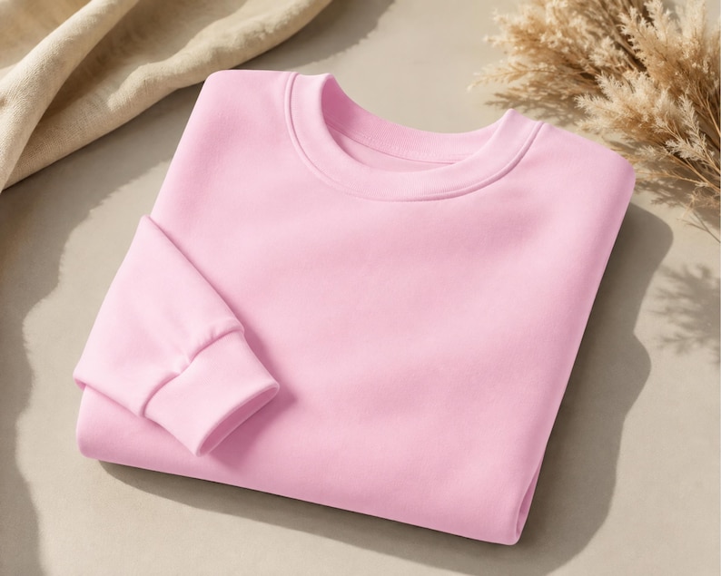 Puede incluir: Una sudadera de cuello redondo en color rosa claro s&oacute;lido, con mangas largas que presentan pu&ntilde;os acanalados y un cuello tambi&eacute;n acanalado. La prenda est&aacute; doblada cuidadosamente, mostrando una textura de tela lisa y uniforme en toda su superficie.