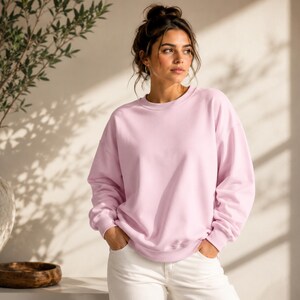 Puede incluir: Una sudadera de cuello redondo en color rosa claro con mangas largas y pu&ntilde;os acanalados, combinada con pantalones blancos. La sudadera presenta un corte relajado, un escote redondo sencillo y un color pastel s&oacute;lido y uniforme.