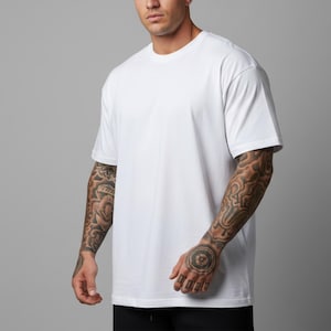 May include: A plain white t-shirt with short sleeves and a crew neck. The shirt has a loose fit. The model is wearing black trousers. The background is a plain grey.