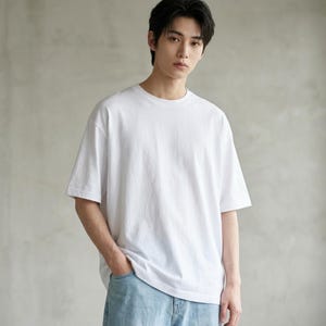 Könnte beinhalten: Ein schlichtes weißes T-Shirt mit kurzen Ärmeln, Rundhalsausschnitt und lockerer Passform, kombiniert mit einer hellblauen Jeans. Das T-Shirt hat ein einfarbiges Design mit einem Standard-Saum und einer einfachen Verarbeitung.