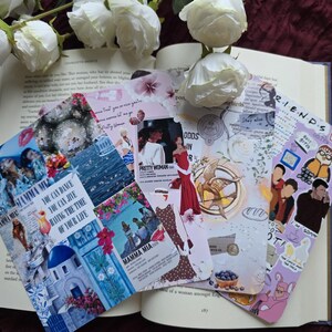 Könnte beinhalten: Eine Sammlung dekorativer Lesezeichen mit Filmplakaten und Zitaten, darunter "Mamma Mia" und "Pretty Woman". Die Lesezeichen liegen auf einem offenen Buch, mit weißen Rosen im Hintergrund.