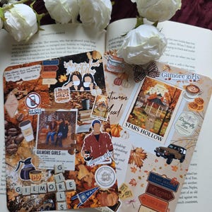 May include: Two decorative paper cutouts with a collage theme, featuring images and text related to the TV show "Gilmore Girls." The cutouts are placed on an open book, with white roses in the background. The color scheme includes browns, oranges, and beige.