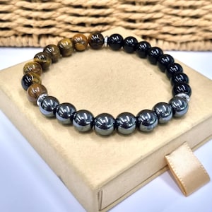 Può includere: Un braccialetto di perline composto da una combinazione di perle rotonde occhio di tigre con bande marroni e dorate, perle di onice nero liscio e perle di ematite grigio metallizzato, con piccoli distanziatori in metallo argentato.