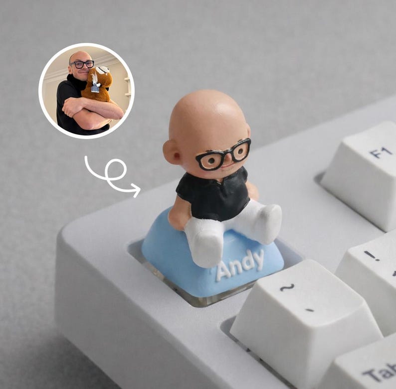 Puede incluir: Una tecla de teclado novedosa con una peque&ntilde;a figura de una persona con gafas y una camisa negra, sentada en una tecla azul claro. La tecla est&aacute; etiquetada como "Andy". La figura est&aacute; en un teclado blanco.