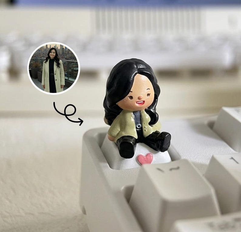 Puede incluir: Una figura en miniatura de una persona con cabello negro y una chaqueta beige sentada en una tecla del teclado. Un peque&ntilde;o coraz&oacute;n rosa est&aacute; al lado de la figura. Una imagen circular de una persona con abrigo est&aacute; en el fondo.