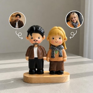 Puede incluir: Un par de figuras personalizadas de una pareja, de pie sobre una base de madera. La figura masculina lleva una chaqueta marrón y pantalones negros, mientras que la figura femenina tiene el pelo rubio y una bufanda. Fotos de la pareja en el fondo.
