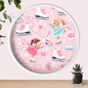 May include: A round wall clock with a white frame. The clock face is pink and features illustrations of ice skates, snowflakes, hearts, and two girls ice skating. The clock hands are white.