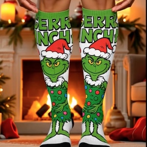 Może przedstawiać: Białe podkolanówki z zielonym Grinchem w czapce Świętego Mikołaja i zielonym stroju w kolorowe kropki. Na górze skarpetek widnieje napis "Merry Grinch!".