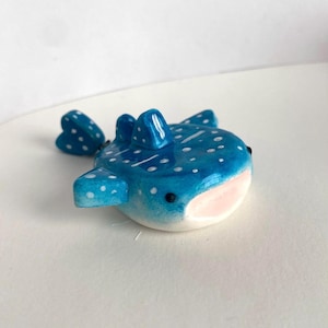Op de afbeelding: Een handgemaakt walvishaai-beeldje in blauw met witte stippen. De keramische sculptuur heeft een afgerond lichaam, kleine vinnen en een roze mond. De walvishaai is een zeedier en dit beeldje is een decoratief item.
