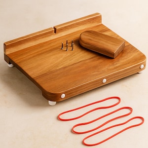 Può includere: Tagliere in legno di forma rettangolare arrotondata, con una piccola maniglia in legno e tre perni metallici. Include tre elastici rossi. La tavola poggia su quattro piedini bianchi.