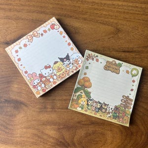 May include: Two square memo pads with lined paper. The left pad features Sanrio characters like Hello Kitty and My Melody with autumn leaves and donuts. The right pad displays Animal Crossing characters, a house, and trees with the game logo.