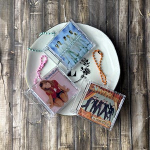 May include: Three square clear plastic miniature CD case keychains with ball chains. One features the Backstreet Boys Millennium album cover, one shows Britney Spears, and one displays the NSYNC No Strings Attached album cover art.