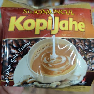 May include: A packet of "Sidomuncul Kopi Jahe" instant coffee mix. The packaging is predominantly brown and gold, with the product name in large yellow letters. The image on the packet shows coffee being poured into a cup.