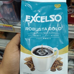 Op de afbeelding: Een blauwgroene en gouden zak Excelso Robusta Gold gemalen koffie. De zak bevat de merknaam en productbeschrijving. Een illustratie van een witte koffiekop met koffiebonen staat op de voorkant. De zak bevat 200 g koffie.