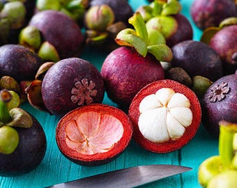 May include: A collection of whole and halved mangosteen fruits featuring deep purple rinds, green stems, and bright white segmented flesh inside. One fruit is sliced open to reveal the vibrant red interior lining and the soft white fruit segments.