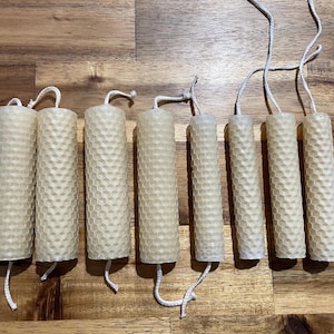 Puede incluir: Siete velas cilíndricas de cera de abeja con un patrón de panal. Las velas son de varias alturas y tienen un color amarillo claro natural. Cada vela tiene una mecha blanca que se extiende desde la parte superior e inferior.