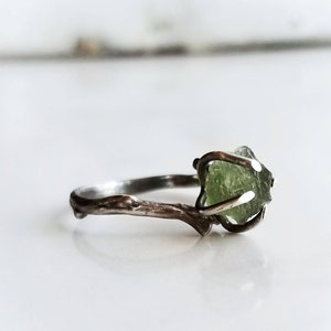 May include: A silver ring with a branch design and a green gemstone set in the center.