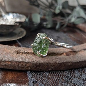 May include: A silver ring with a green peridot gemstone set in a branch-like band.
