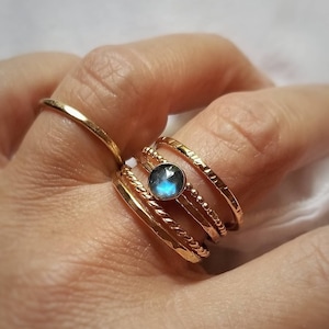 May include: A set of five gold rings with a blue gemstone in the center. The rings are stacked on top of each other and have different textures.